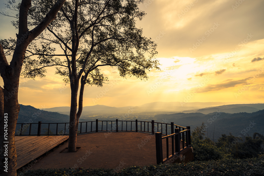 The wooden balcony has a view of the mountains and sunset behind.