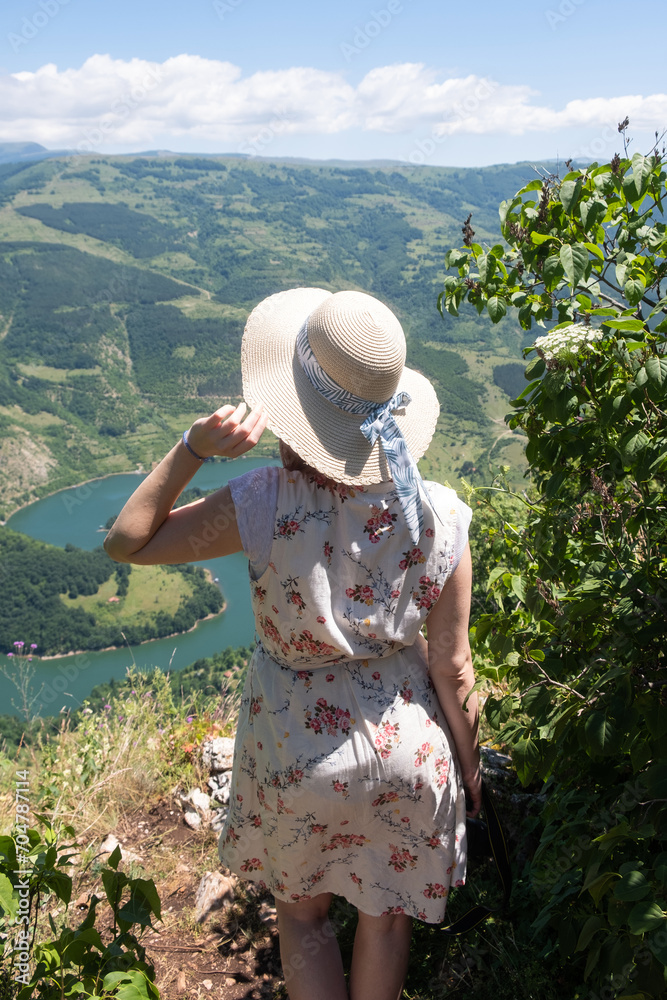 A woman in a hat from behind enjoying the mountain view