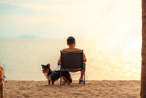 Dog owner sitting on a chair on the beach and see sunset.