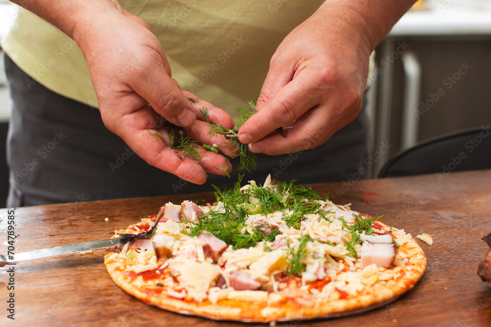 Sprinkle herbs on pizza. Male hands add dill to pizza.