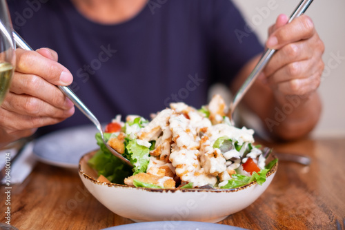 Woman with plate of delicious tempting Caesar salad on wooden table holds two spoons for sharing lunch, healthy eating concept