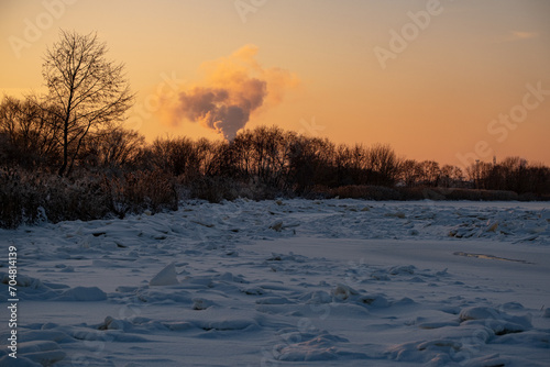 Winter landscape with smoke from the chimney of an industrial plant. Landscape with golden sunset light in cold winter evening in Latvia © Neils