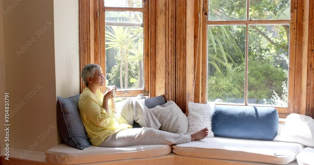 Happy senior biracial woman sitting on couch and drinking tea at home, slow motion Happy senior biracial woman sitting on couch and drinking tea at home, slow motion