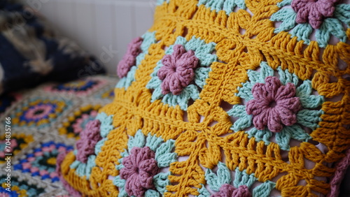 close-up of a crochet cushion with colorful flowers on a bed.