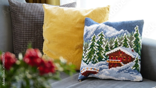 handmade cross-stitch snow-themed cushion and grey and yellow pillows on the couch in the wintertime.