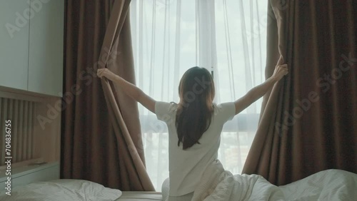 happy woman stretching on bed after wake up, young adult female rising arms and looking to window in the early morning. fresh relax and have a nice day concepts photo