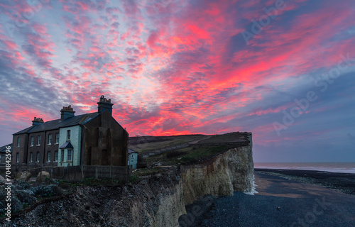 Dramatic dawn sky over the precarious cottages on the cliff edge of Birling Gap on the south downs east Sussex coast south east England UK photo