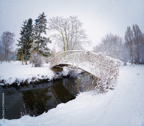 Calm winter view of pedestrian bridge on Seret river in Topilche park, Ternopil town, Ukraine, Europe. Snowy winter scene of city park. Traveling concept background.. photo