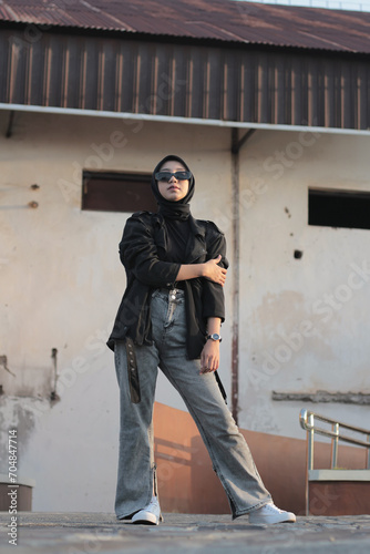 A young Asian woman wearing a hijab and jeans posing outdoors, following a concept with a black outfit