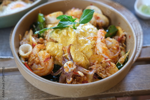 traditional Thai food know as spicy Tom Yum Kung Fried Rice, topped with omelet. Ingredients include galangal, lemongrass, kaffir lime leaves, basil leaves, eggs, chilli, shrimp and squid.