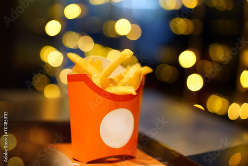 French fries or fried potatoes in a red carton box against background of Christmas garlands photo