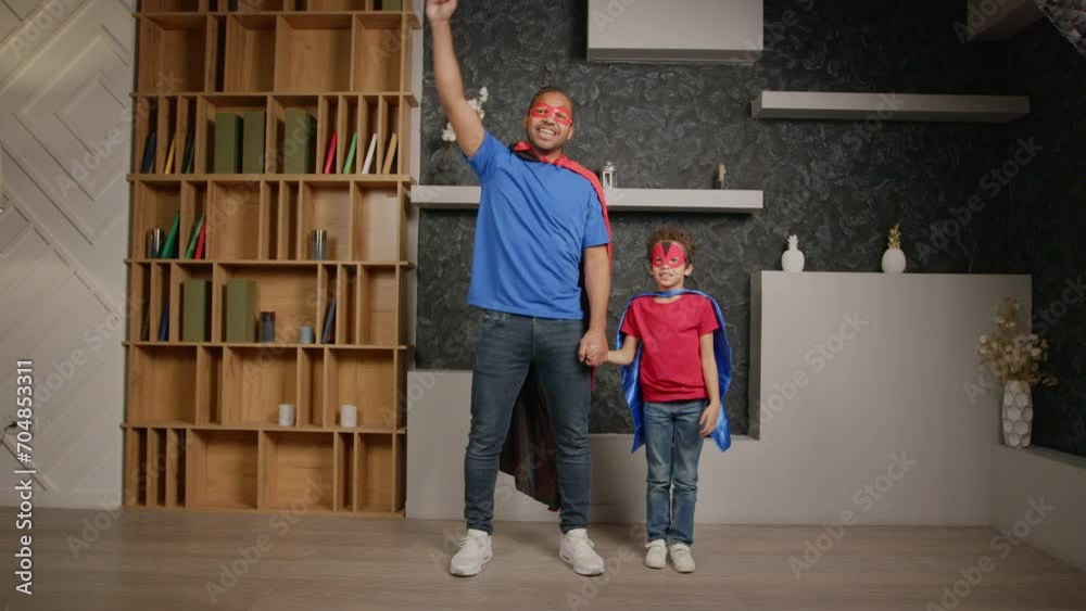 Joyful playful African American family in superhero capes and masks having fun playing , jumping with one arm raised up, showing carefree mood and happiness while enjoying leisure at home. Joyful playful African American family in superhero capes and masks having fun playing , jumping with one arm raised up, showing carefree mood and happiness while enjoying leisure at home.