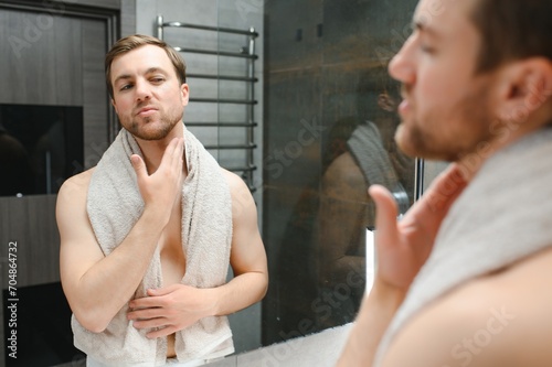 Young man looking in mirror after shaving at home photo