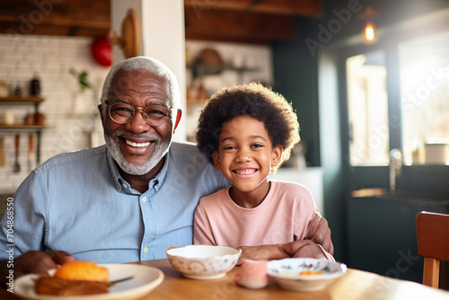Smiling African American grandfather and grandson, senior or old man sitting at table, eating and talking with little boy, selective focus