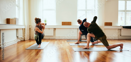 Yoga instructor teaching a group of male students the crescent lunge on knee pose during a class in a studio photo