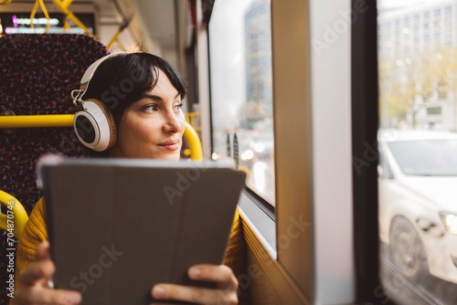 Woman wearing wireless headphones and sitting with tablet PC in bus photo