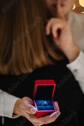 A man hugs a woman and hides a ring from her. A surprise marriage proposal. Man making a surprise with a wedding ring. Blurred romantic couple in love. Engagement ring closeup. photo