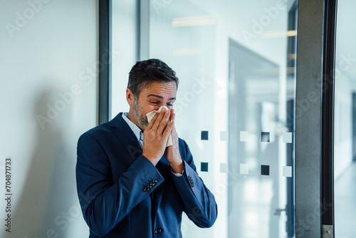 Businessman blowing nose on handkerchief in office photo
