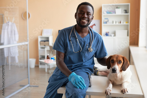 Smiling veterinarian sitting with beagle dog on table in clinic photo
