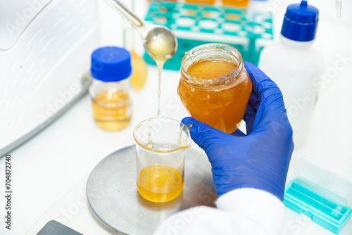 Hand of scientist weighing honey in measuring beaker at laboratory photo