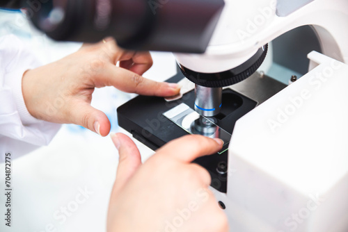 Hands of microbiologist positioning sample in microscope photo