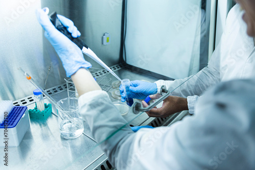 Scientist with colleague taking liquid solution with pipette photo