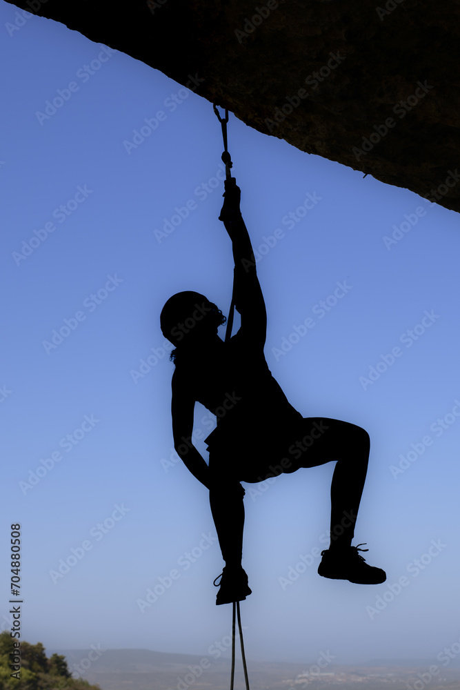 Image of a determined and brave girl climbing an imposing rock face. With an expression of concentration on her face, she holds on to the rope with determination.