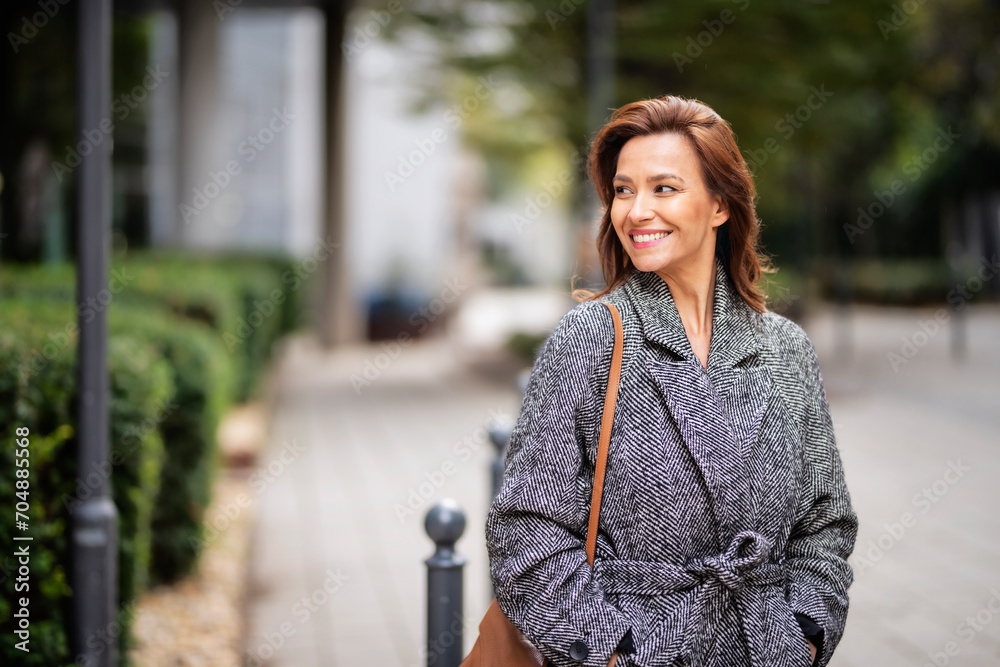 Brunette haired woman wearing tweend coat and walking outdoors in the city street on autumn day