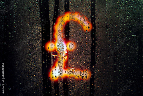 Blurred glowing English pound sign made from light bulbs.The symbol of the national currency behind a rain-wet window with water drops in the night.Sign of economic crisis and business problems photo