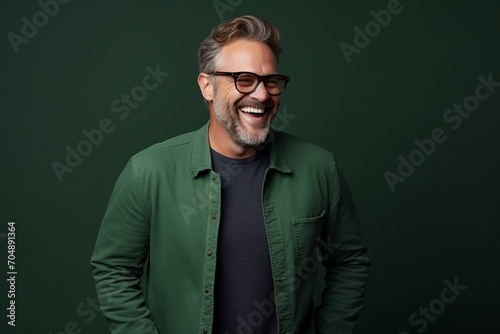 Portrait of happy mature man in eyeglasses smiling at camera while standing against green background