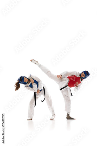 Full-length image of young competitive girls in dobok and helmet, practicing taekwondo, training isolated over white background. Concept of martial arts, combat sport, competition, action