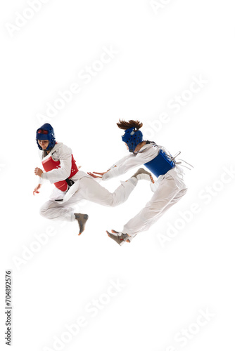 Two young girls in dobok and helmet training, practicing taekwondo poses, stances isolated over white background. Concept of martial arts, combat sport, competition, action