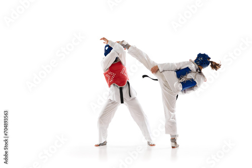 Kick and protection stunts. Young girls, taekwondo athletes in motion, practicing isolated over white background. Concept of martial arts, combat sport, competition, action, school