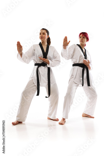 Full-length images of young girls in kimono and black belts, karate, taekwondo, judo athletes standing in poses against white background. Concept of martial arts, combat sport, competition, action