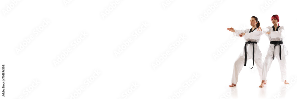 Young girls in kimono and black belts, karate, taekwondo, judo athletes standing isolated over white background. Concept of martial arts, combat sport, competition. Banner. Empty space to insert text Young girls in kimono and black belts, karate, taekwondo, judo athletes standing isolated over white background. Concept of martial arts, combat sport, competition. Banner. Empty space to insert text