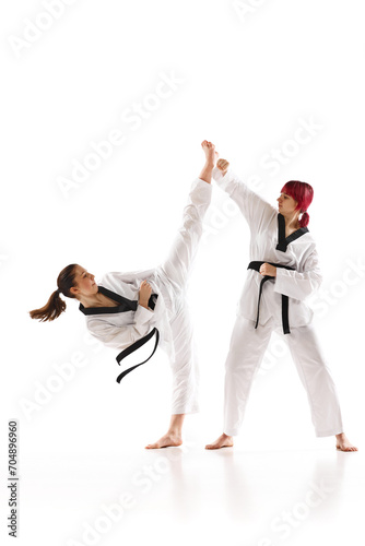 Young sportive girls in kimono and black belted practicing karate, judo, taekwondo stunts isolated over white background. Concept of martial arts, combat sport, competition, action