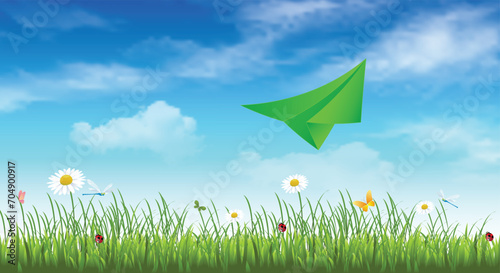 Green paper airplane on a blue sky background with clouds, green grass and flowers. Spring background. Travel banner. copy space. © Iryna