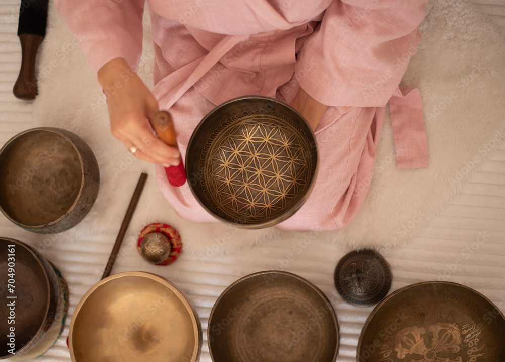 Fototapeta premium Woman in pink clothes hold sound metal bowl and make music in spa salon. Yoga for health, relaxation and meditation body, practice for forgiveness and spiritual harmony.