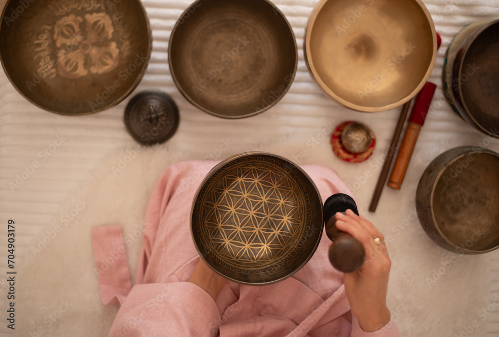 Fototapeta premium Woman in pink clothes hold sound metal bowl and make music in spa salon. Yoga for health, relaxation and meditation body, practice for forgiveness and spiritual harmony.