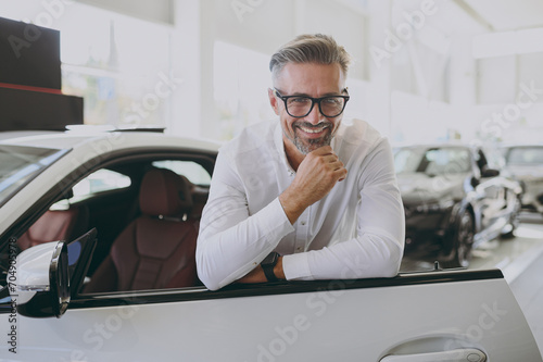 Adult man customer male buyer client wearing shirt glasses open lean on door prop up chin choose auto want buy new automobile in car showroom vehicle salon dealership store motor show. Sales concept. photo