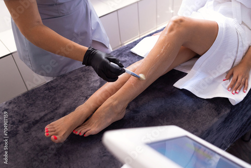 Preparation of clients legs before laser hair removal procedure in spa salon.