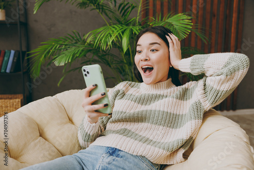 Φωτογραφία Young surprised shocked woman in casual clothes sits on armchair hold in hand us