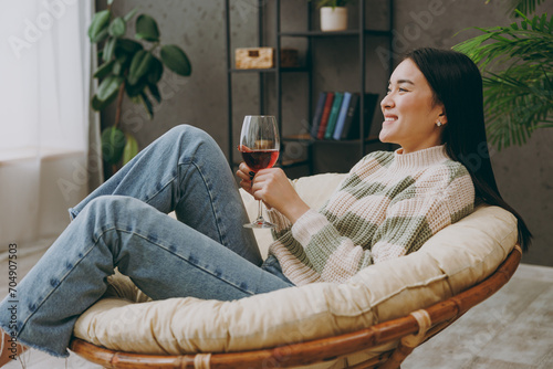 Side view young smiling fun happy woman she wearing casual clothes drink red wine sits on armchair stay at home hotel flat rest relax spend free spare time in grey living room indoor. Lounge concept. #704907503