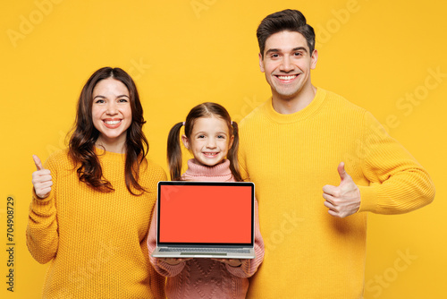Young IT parents mom dad child kid girl 7-8 years old wear sweater casual clothes hold use work on blank screen laptop pc computer show thumb up isolated on plain yellow background Family day concept