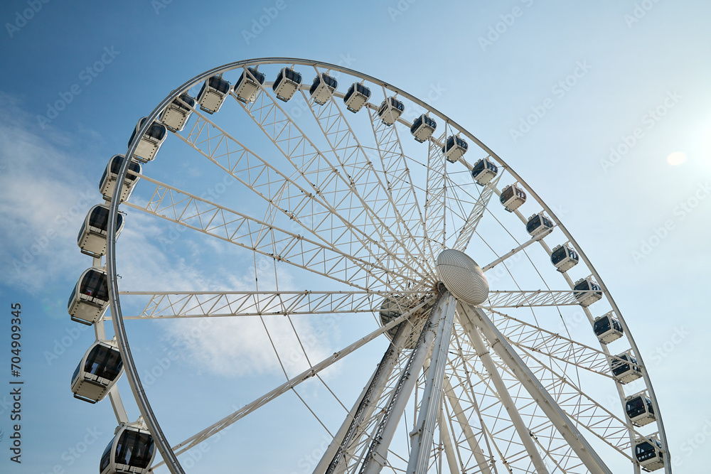 Ferris wheel rotates against background of blue cloudy sky. Amusement park attraction. Summer holidays