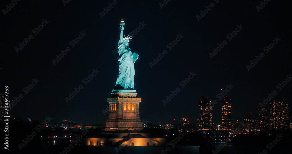 Aerial View of the Illuminated Statue of Liberty. Iconic Travel Destination and Tourist Attraction with Manhattan and Brooklyn Office Buildings All Lit Up at Night. Nightlife in New York City