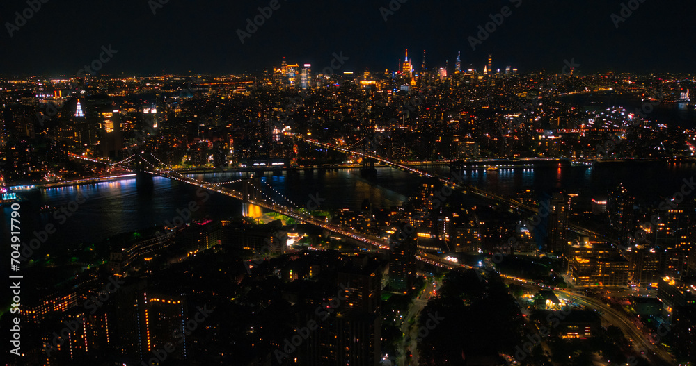 Iconic New York City Nightlife Landscape Over East River with Skyscrapers, Manhattan and Brooklyn Bridges, Cars and Ferry Boats. Cinematic Night Urban Skyline with Office Buildings with Lights