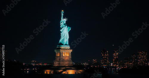 Aerial View of the Illuminated Statue of Liberty. Iconic Travel Destination and Tourist Attraction with Manhattan and Brooklyn Office Buildings All Lit Up at Night. Nightlife in New York City photo