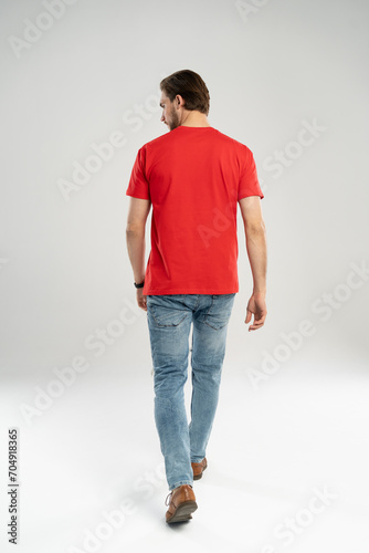 Man in jeans and red t-shirt is walking. Rear view. Full length studio shot isolated on white