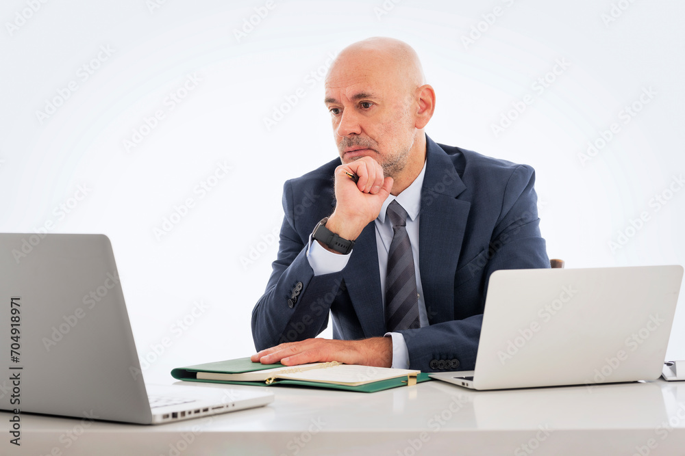 Thinking businessman sitting at desk and using laptops against isolated white background Thinking businessman sitting at desk and using laptops against isolated white background